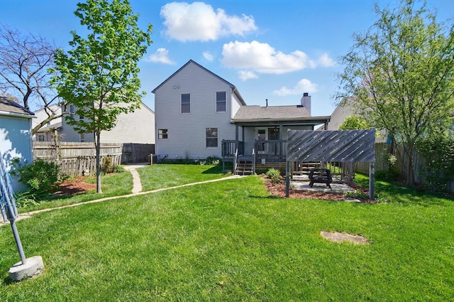 rear view of house featuring fence, a deck, a chimney, a lawn, and a patio