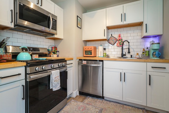 kitchen featuring butcher block countertops, backsplash, a sink, stainless steel appliances, and light wood-style flooring