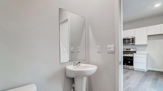 half bath featuring toilet, baseboards, a sink, and wood finished floors