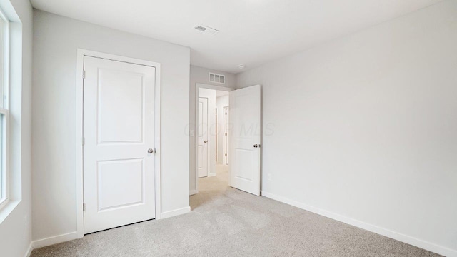 unfurnished bedroom featuring baseboards, visible vents, and light carpet