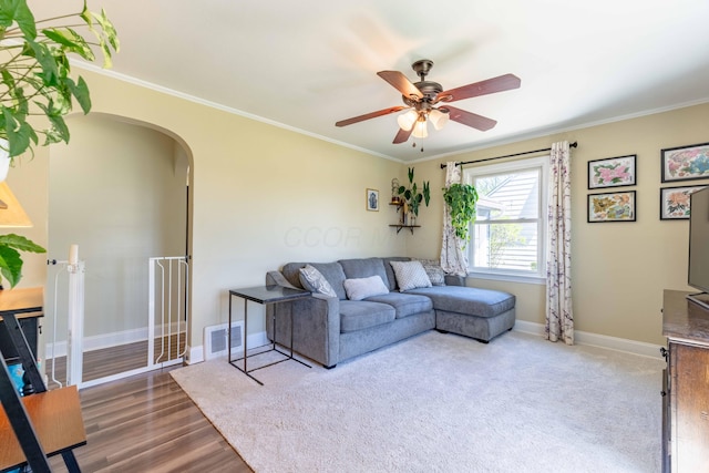 living area with arched walkways, ceiling fan, baseboards, and ornamental molding
