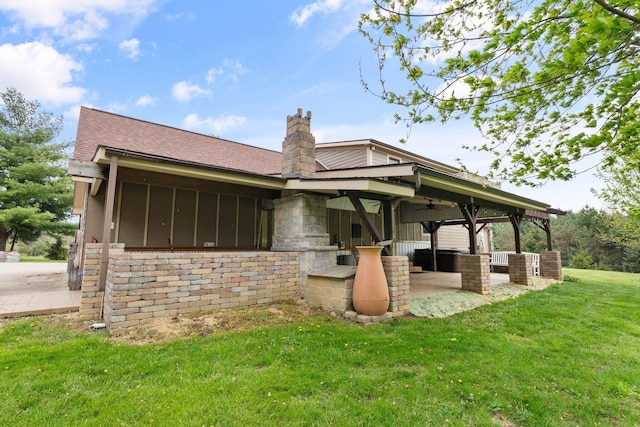 rear view of house with a patio, a chimney, a ceiling fan, a shingled roof, and a lawn