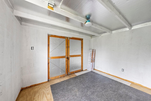 spare room with baseboards, beam ceiling, and wood finished floors