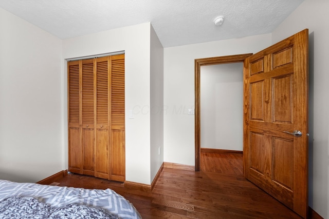 bedroom with dark wood-style flooring, baseboards, and a closet