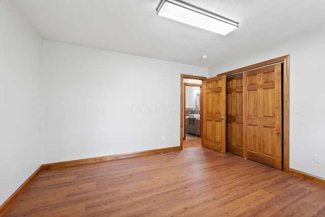 unfurnished bedroom featuring a textured ceiling, baseboards, wood finished floors, and a closet