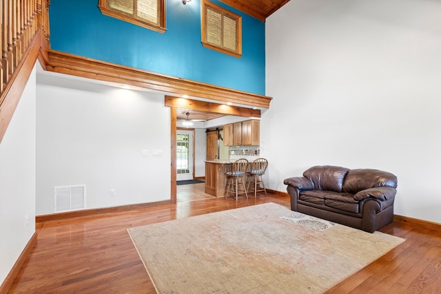 living area with high vaulted ceiling, baseboards, wood finished floors, and visible vents