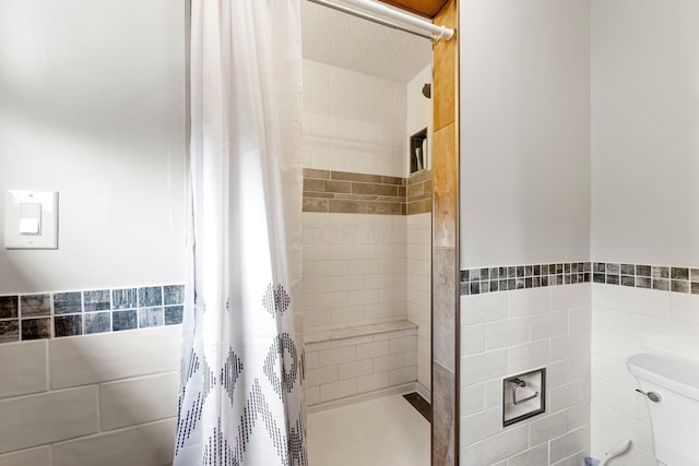 bathroom featuring wainscoting, tile walls, toilet, and tiled shower