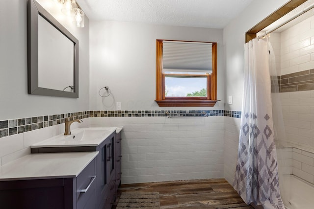 bathroom featuring vanity, wood finished floors, tile walls, a wainscoted wall, and a tile shower