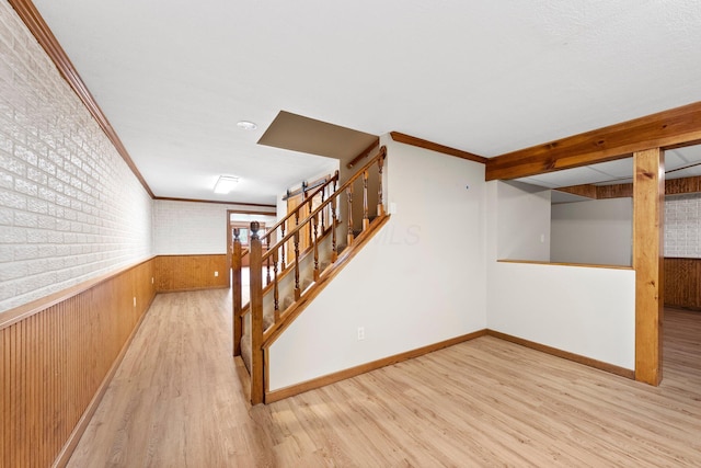 interior space featuring ornamental molding, wood finished floors, wooden walls, stairway, and a wainscoted wall