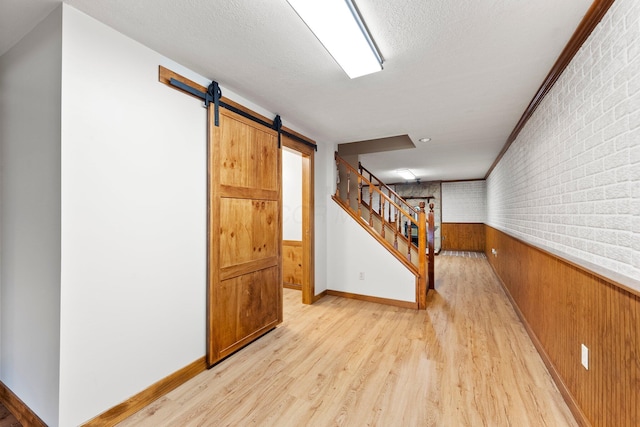 basement with wood walls, wainscoting, light wood-type flooring, and a barn door