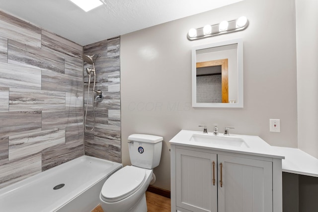 bathroom with toilet, tiled shower, and vanity