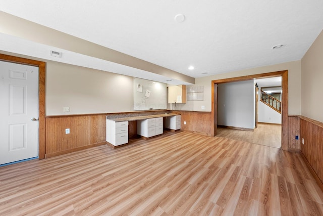 kitchen with visible vents, wooden walls, built in desk, a wainscoted wall, and light wood finished floors