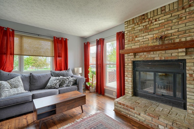 living room with wood-type flooring, a textured ceiling, and a brick fireplace