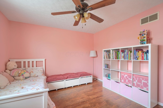 bedroom with ceiling fan, a textured ceiling, baseboards, wood finished floors, and visible vents