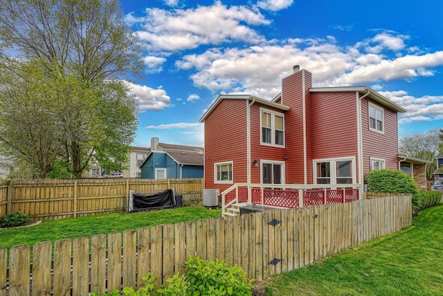 rear view of property featuring a chimney, a deck, central air condition unit, a fenced backyard, and a yard