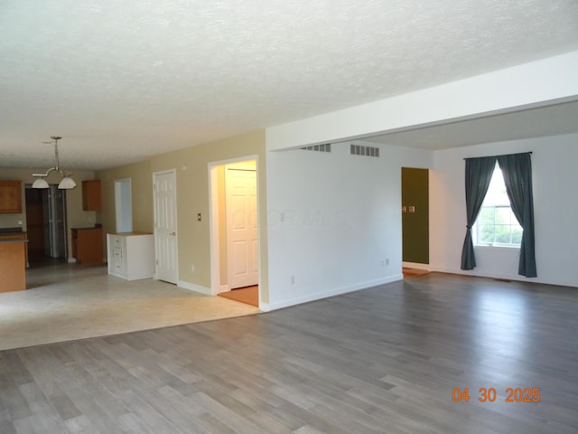 unfurnished living room featuring visible vents, a textured ceiling, wood finished floors, and a notable chandelier