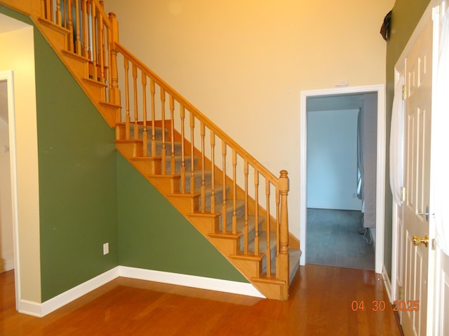 stairway featuring baseboards, a high ceiling, and wood finished floors