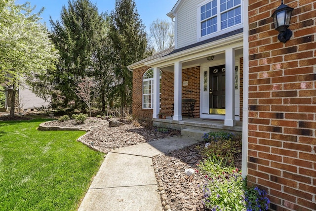 view of exterior entry featuring brick siding, a lawn, and a porch