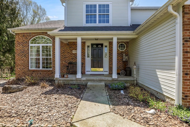 view of exterior entry featuring a porch, brick siding, and a shingled roof