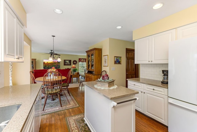 kitchen featuring freestanding refrigerator, decorative backsplash, dark wood-style flooring, a kitchen island, and white cabinetry