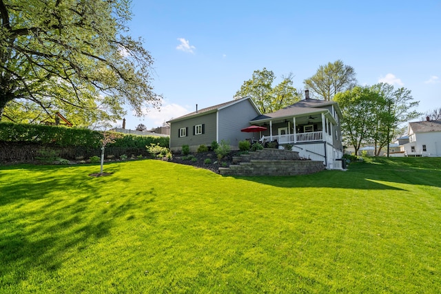 rear view of property with a porch, ceiling fan, and a yard