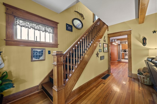 staircase with baseboards, beamed ceiling, hardwood / wood-style flooring, and visible vents