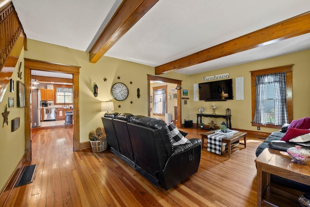 living area with light wood-style floors, baseboards, beamed ceiling, and visible vents