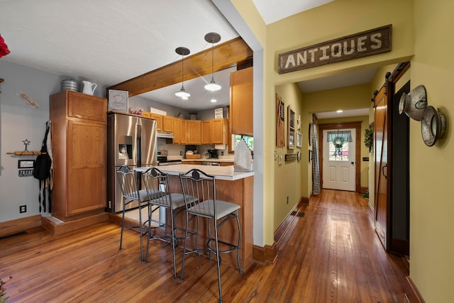 kitchen featuring a kitchen breakfast bar, a peninsula, dark wood-style floors, under cabinet range hood, and stainless steel appliances