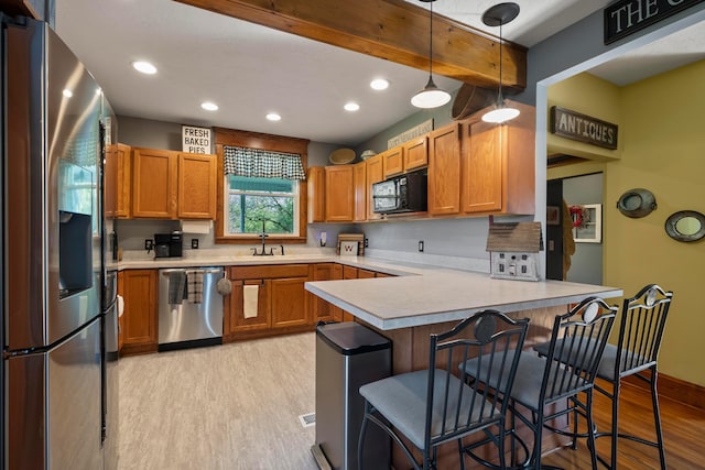 kitchen featuring appliances with stainless steel finishes, a sink, light countertops, a peninsula, and light wood-style floors