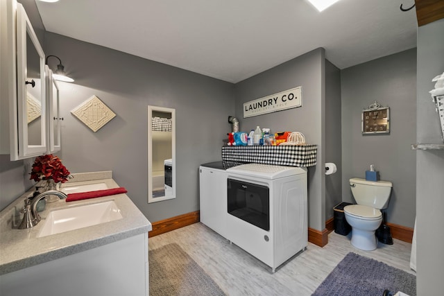 laundry room with laundry area, baseboards, light wood-style floors, washer and clothes dryer, and a sink