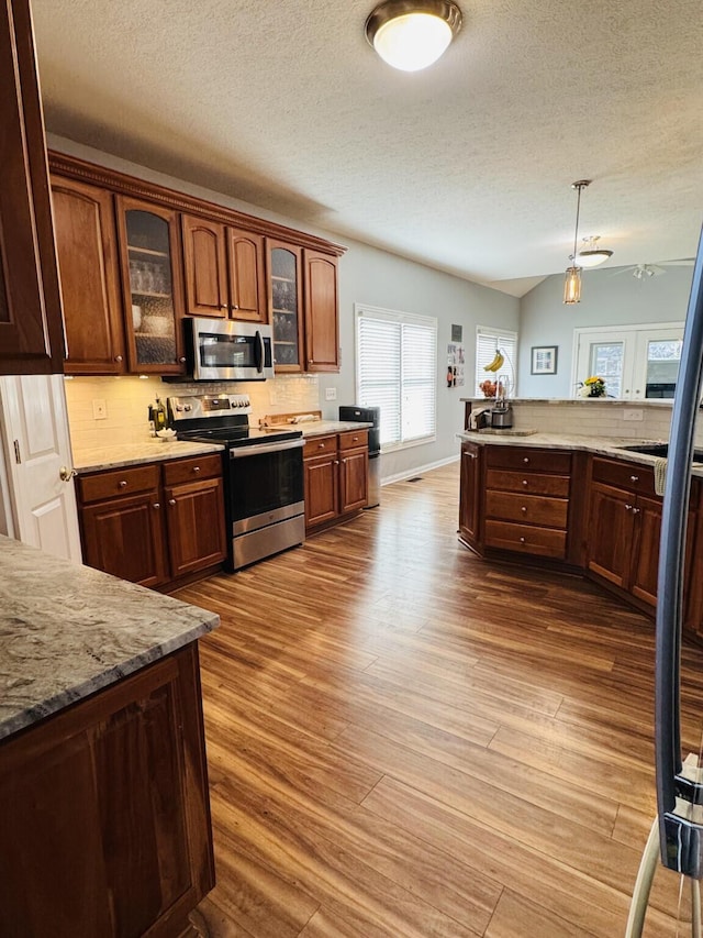kitchen with wood finished floors, glass insert cabinets, a textured ceiling, tasteful backsplash, and stainless steel appliances