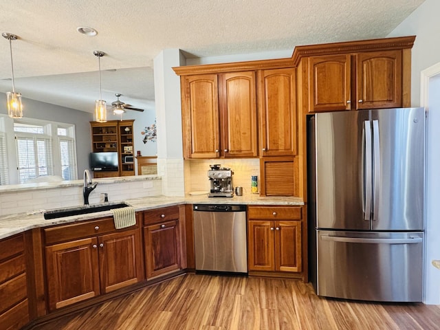 kitchen with stainless steel appliances, light stone countertops, a sink, and wood finished floors