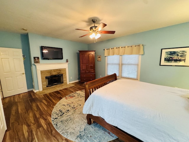 bedroom with baseboards, a ceiling fan, a stone fireplace, and wood finished floors