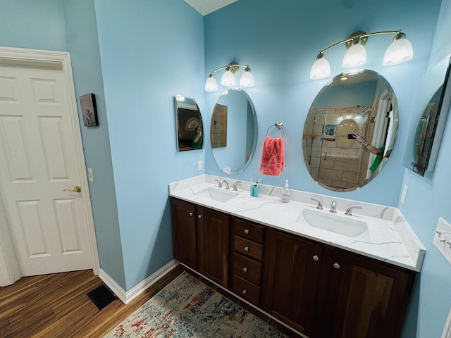 bathroom featuring visible vents, a sink, wood finished floors, and tiled shower