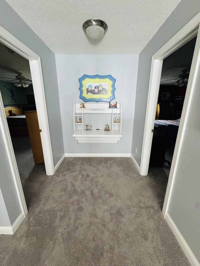 hall with a textured ceiling, baseboards, and carpet
