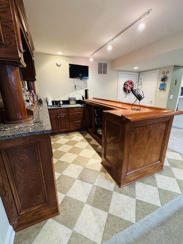 bar with a textured ceiling, visible vents, track lighting, and bar