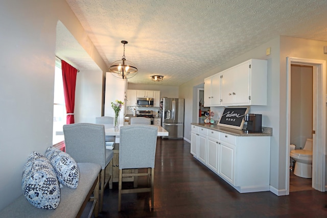 kitchen with a textured ceiling, white cabinets, dark wood-style floors, an inviting chandelier, and stainless steel appliances