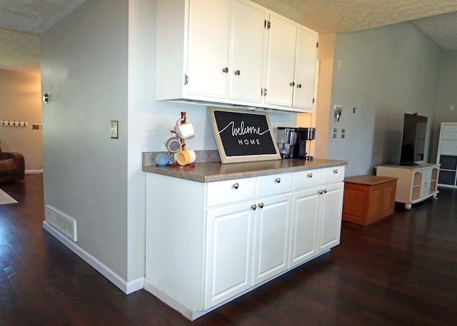 kitchen featuring a textured ceiling, visible vents, baseboards, white cabinets, and dark wood-type flooring
