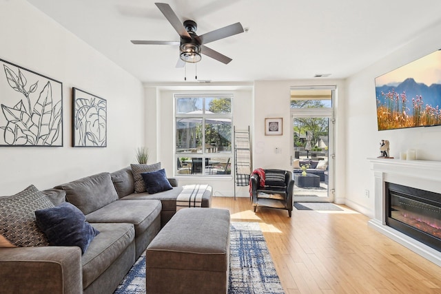 living area featuring a ceiling fan, a glass covered fireplace, hardwood / wood-style flooring, and visible vents