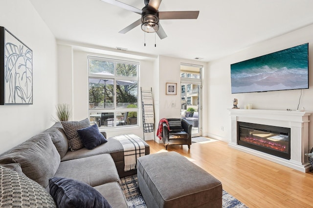 living room with ceiling fan, a glass covered fireplace, wood finished floors, and visible vents
