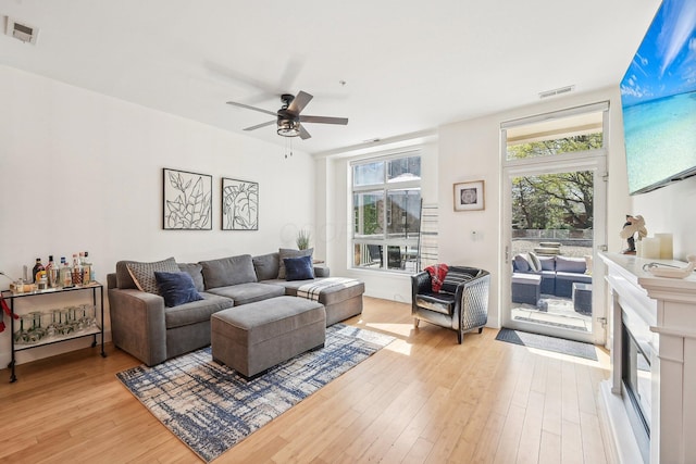 living area with visible vents, a ceiling fan, light wood-style floors, and a glass covered fireplace