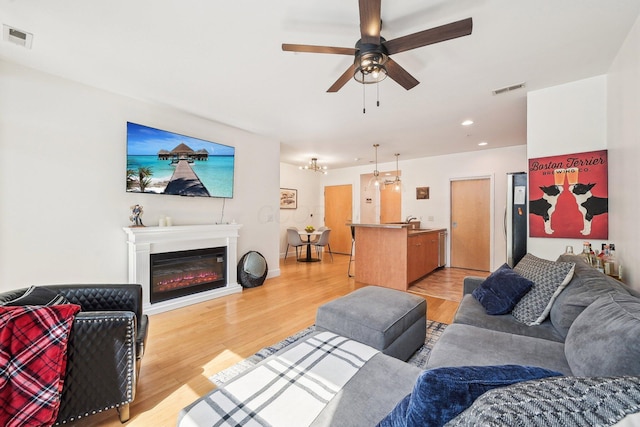 living room with visible vents, a ceiling fan, light wood finished floors, and a glass covered fireplace