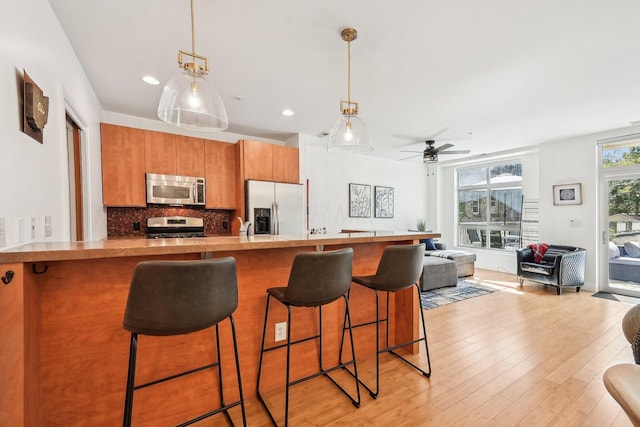 kitchen featuring open floor plan, a kitchen bar, brown cabinets, hanging light fixtures, and stainless steel appliances