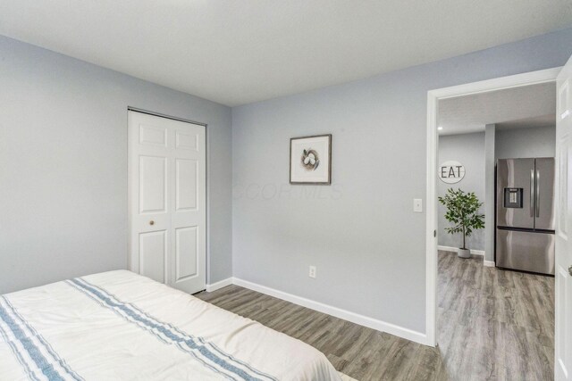 bedroom with stainless steel refrigerator with ice dispenser, light wood finished floors, and baseboards