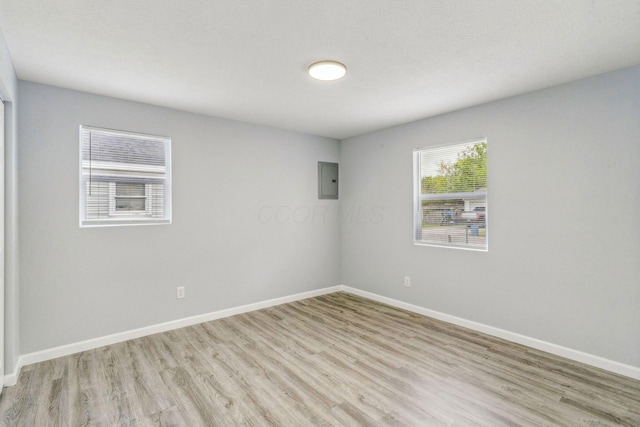 unfurnished room featuring baseboards, electric panel, and light wood-type flooring