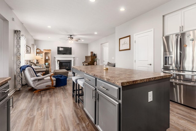kitchen with wood finished floors, ceiling fan, a breakfast bar area, stainless steel fridge, and a center island