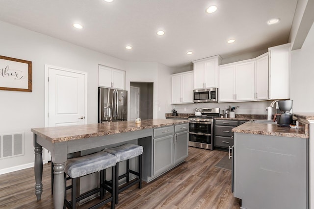 kitchen with visible vents, a kitchen island, dark wood-style floors, a sink, and stainless steel appliances