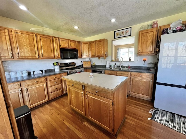 kitchen with a textured ceiling, gas range, black microwave, a sink, and freestanding refrigerator
