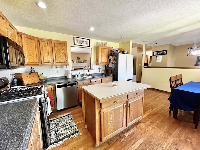 kitchen featuring stainless steel appliances, a textured ceiling, a sink, and light wood-style flooring