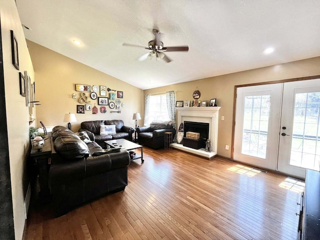 living area with a fireplace with raised hearth, french doors, hardwood / wood-style floors, a ceiling fan, and lofted ceiling